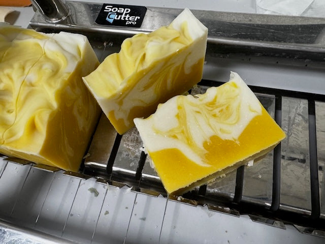 Three yellow and white swirled soap bars on a loaf cutter.