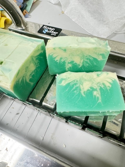 Three green soap bars with white swirls on a professional soap cutter. 