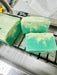 Three green soap bars with white swirls on a professional soap cutter. 