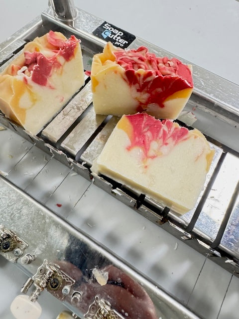 Three soap bars with pink and white marbled design on a metal soap cutter.